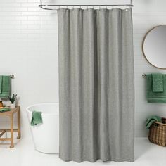 a white bath tub sitting under a bathroom mirror next to a shower curtain with green towels on it