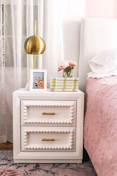 a white nightstand with two books on top of it next to a pink bedspread