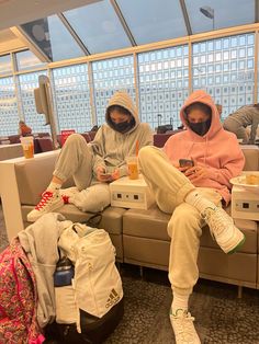 two people sitting on a couch in an airport terminal, one with a cell phone