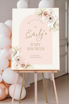 a baby shower sign sitting on top of a easel next to balloons and flowers