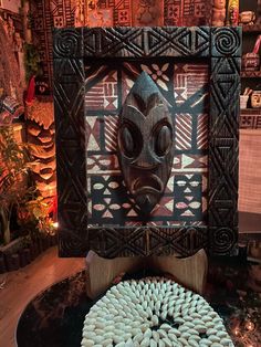 a cake with white frosting in front of a wooden frame and an african mask