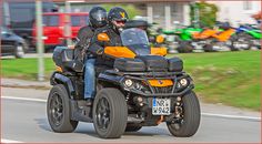 two people riding on the back of an orange and black four - wheeled vehicle down a street