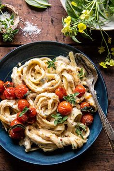 pasta with tomatoes and cream sauce on a blue plate next to a flowery bouquet