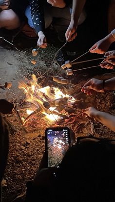 a group of people sitting around a campfire with marshmallows on sticks