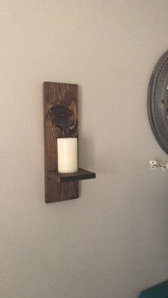 a candle is sitting on a wooden shelf next to a wall mounted clock and mirror