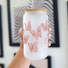 a person holding a glass jar with pink butterflies on it and a straw sticking out of the lid