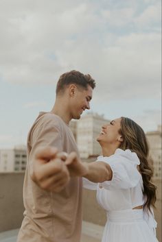 a man and woman dancing on the roof of a building with buildings in the background