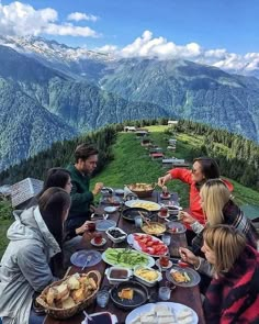 a group of people sitting at a table with food in front of them on top of a mountain