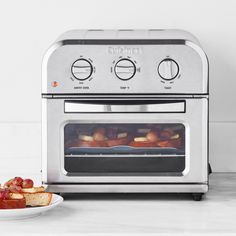 a toaster oven with food cooking in it next to a plate on the counter