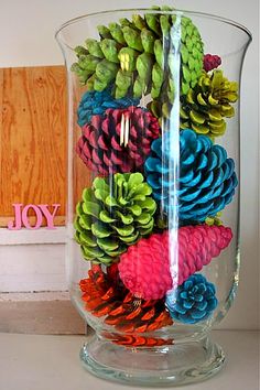 pine cones and other decorations in a glass vase on a table next to a wooden sign