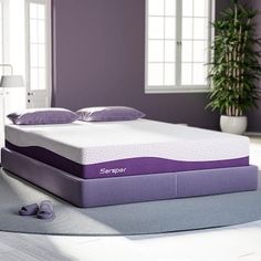 a purple and white mattress sitting on top of a bed in a room with windows