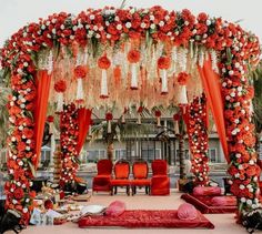 an outdoor wedding setup with red and white flowers on the altar, orange draping