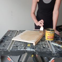 a woman is using a brush to paint a piece of wood on top of a workbench