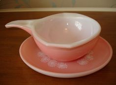 two pink dishes sitting on top of a wooden table next to a white bowl and saucer