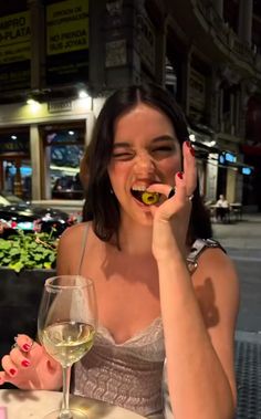 a woman sitting at a table with a glass of wine in front of her mouth