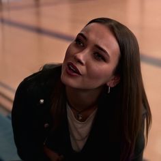 a woman sitting on the floor with her hand up to her face and looking off into the distance