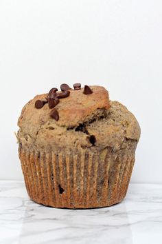 a chocolate chip muffin sitting on top of a marble counter next to a white wall