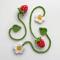 two crocheted strawberries and one flower on a white surface with green stems