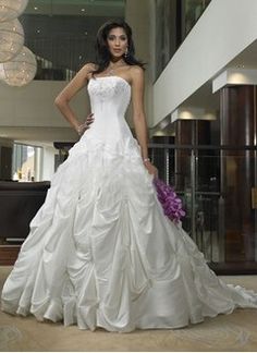 a woman in a white wedding dress standing next to a chandelier and stairs