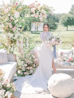 a woman in a white dress standing under an arch with flowers and greenery on it