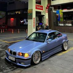 a blue bmw is parked in front of a gas station with its hood up and the door open