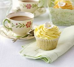 cupcakes and teacups are sitting on the table with white linen napkins