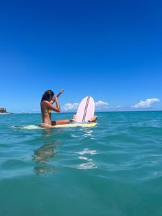 a woman sitting on a surfboard in the ocean with her hand up to her face