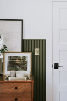 a wooden dresser with a framed photograph on it next to a white door and green striped wall