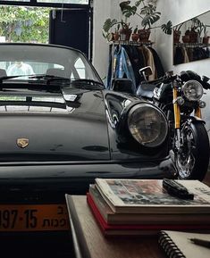 a motorcycle is parked next to a car in a room with plants and books on the table