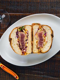 two halves of a sandwich on a white plate next to a wine glass and utensil