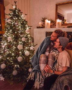 two people sitting on a couch in front of a christmas tree with lights and decorations