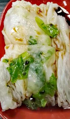 a red plate topped with pasta covered in cheese and sauce on top of green peppers