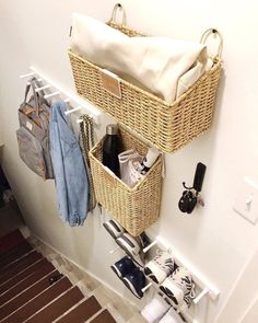 two wicker baskets hanging on the wall with clothes and shoes in them next to a coat rack