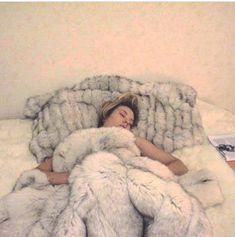 a woman is sleeping in a bed with white furs