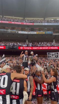 a group of people standing around each other in front of a crowd holding up a trophy