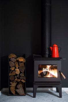 there is a wood burning stove next to a pile of logs and a red teapot