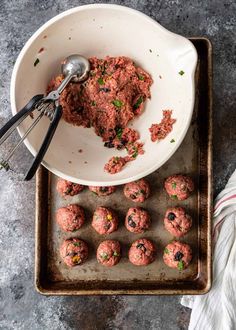 a white bowl filled with meatballs next to a metal ladle on top of a baking sheet