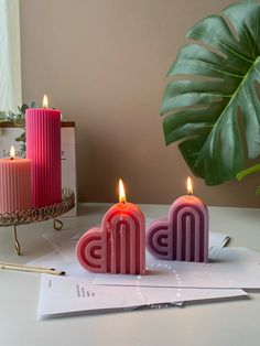 two candles sitting on top of a white table next to a plant and letter m