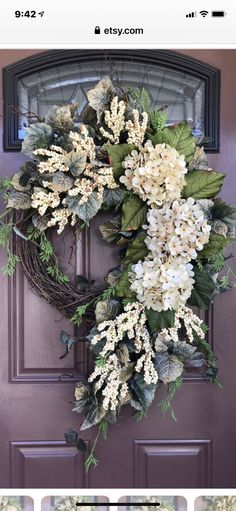 a wreath with purple and white flowers hanging on the front door to welcome guests into the house