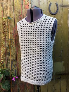 a white crocheted sweater on a mannequin next to a wooden wall