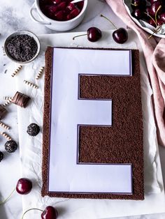 a cake with chocolate frosting and cherries next to the letter e on a table