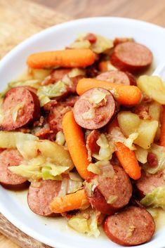 a white bowl filled with sausage, potatoes and carrots on top of a wooden table