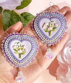 a pair of heart shaped earrings with flowers painted on the front and back of them