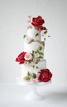 a three tiered white cake with red and pink flowers