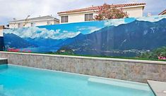 an outdoor swimming pool in front of a house with mountains painted on the wall behind it