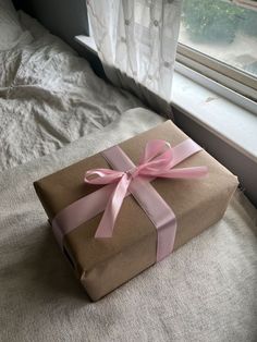 a wrapped gift box sitting on top of a bed next to a window with curtains