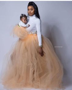 a woman in a white top and tan tulle skirt holding a small baby girl