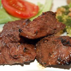 some meat and broccoli on a plate next to a tomato, lettuce and cucumber