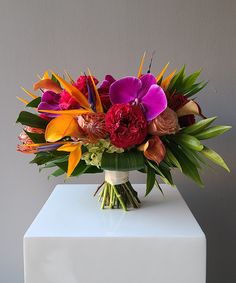 a vase filled with lots of colorful flowers on top of a white countertop next to a gray wall