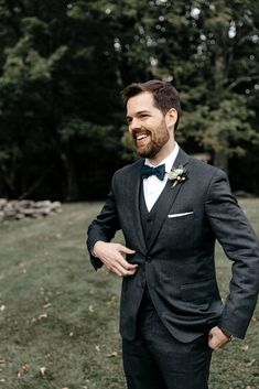 a man in a tuxedo smiles as he stands in the grass with his hands on his hips